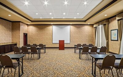 Meeting room arranged in a classroom-style layout with tables, chairs, a projection screen, and a presentation podium at Comfort Suites Frisco.