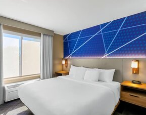 King guest room featuring a comfortable king bed, modern blue accent wall, bedside lighting, and natural light at Comfort Suites Vacaville-Napa Valley Area.
