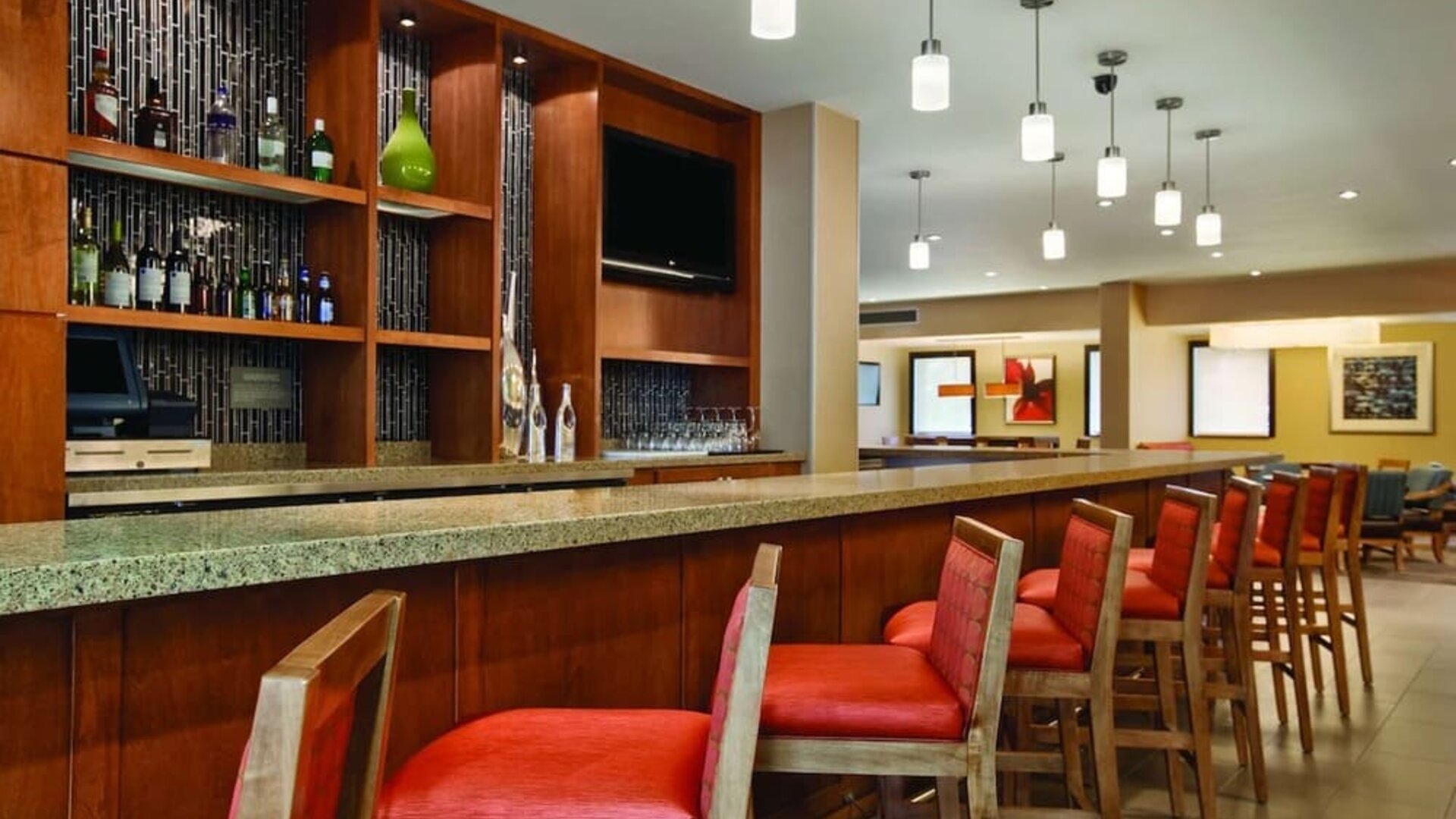 Contemporary hotel bar featuring countertop seating, pendant lighting, beverage displays, and a flat-screen television at Hyatt Place San Jose Downtown.