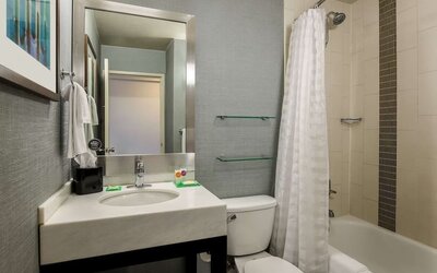 Guest bathroom featuring a modern vanity, large mirror, toilet, and bathtub with shower at Hyatt Place San Jose Downtown.