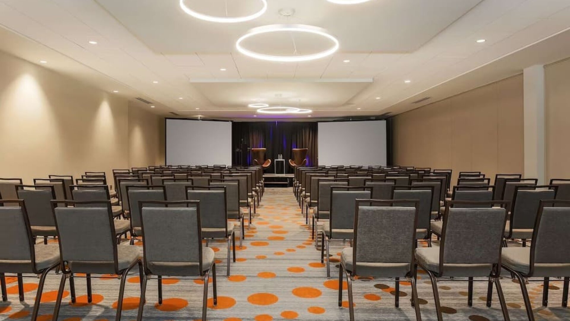 Spacious meeting facility arranged theatre-style with rows of chairs, presentation screens, and a stage area at Hyatt Place San Jose Downtown.