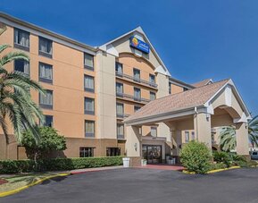 Exterior view of the multi-storey hotel featuring a covered entrance, landscaped grounds, and palm trees at Comfort Inn Southwest At Westpark.