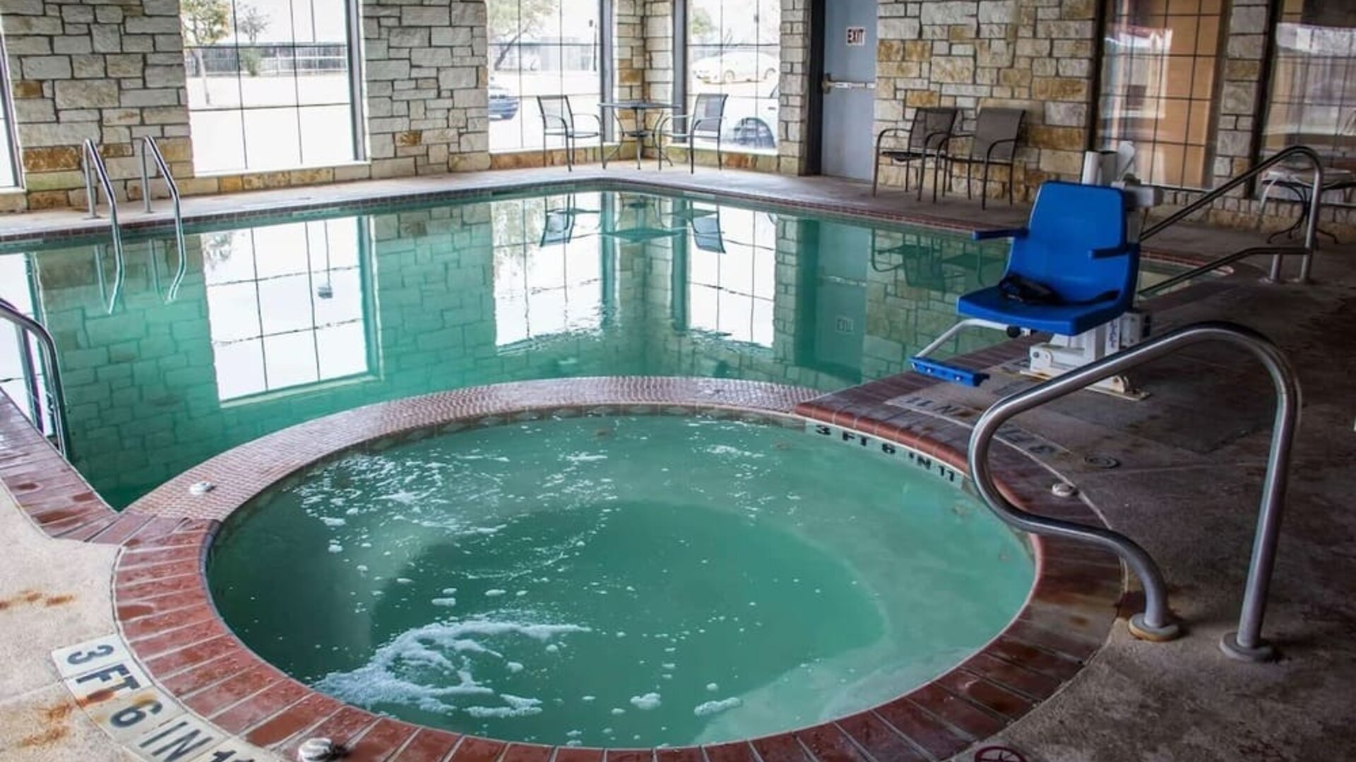 Indoor swimming pool and hot tub with accessibility lift, poolside seating, and large windows at Comfort Suites San Antonio SeaWorld - Lackland AFB.