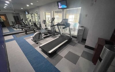 Spacious fitness centre with cardio equipment, mirrored wall, televisions, and large windows at Comfort Suites San Antonio SeaWorld - Lackland AFB.