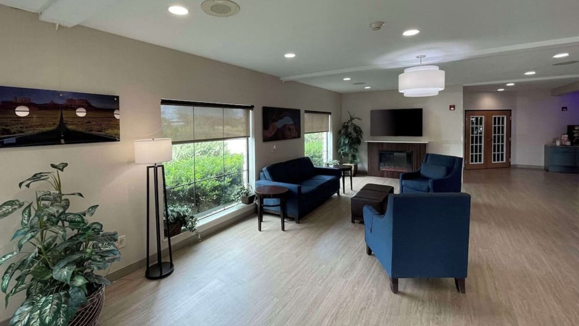Spacious hotel lobby with blue sofas and armchairs, television, floor lamps, plants, and large windows at Comfort Suites San Antonio SeaWorld - Lackland AFB.