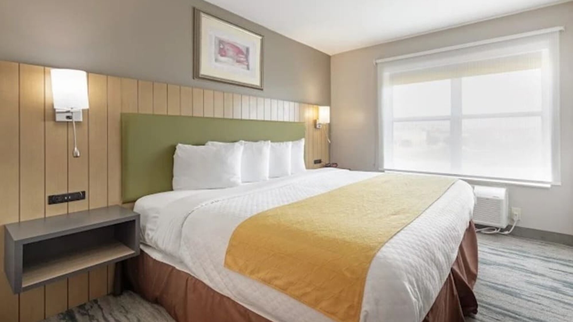 Guest room with king bed, white bedding, green upholstered headboard, bedside lighting, and large window at SureStay by Best Western Lewisville Dallas.