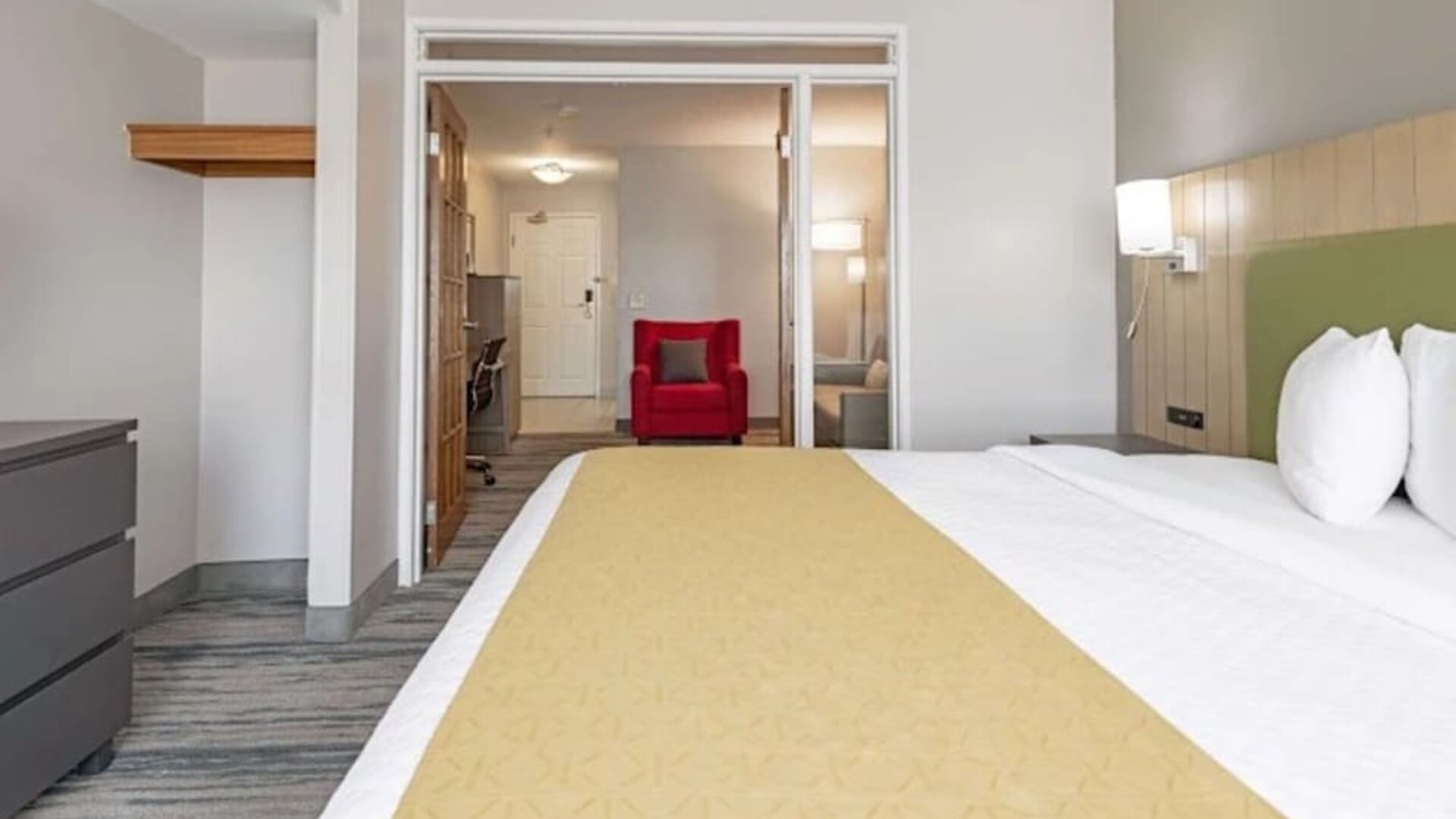 King guest room with white bedding, yellow bed runner, green headboard, and adjoining seating and workspace area at SureStay by Best Western Lewisville Dallas.
