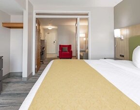 King guest room with white bedding, yellow bed runner, green headboard, and adjoining seating and workspace area at SureStay by Best Western Lewisville Dallas.