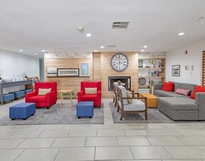 Hotel lobby with sofas, red armchairs, ottomans, fireplace, wall clock, and lounge seating at SureStay by Best Western Lewisville Dallas.
