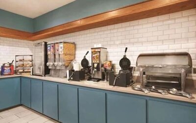Breakfast station with waffle makers, cereal dispensers, pastries, and hot-food service area at SureStay by Best Western Lewisville Dallas.