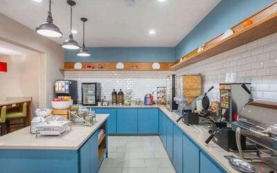 Breakfast buffet with waffle makers, cereal dispensers, hot-food station, beverages, and blue cabinetry at SureStay by Best Western Lewisville Dallas.