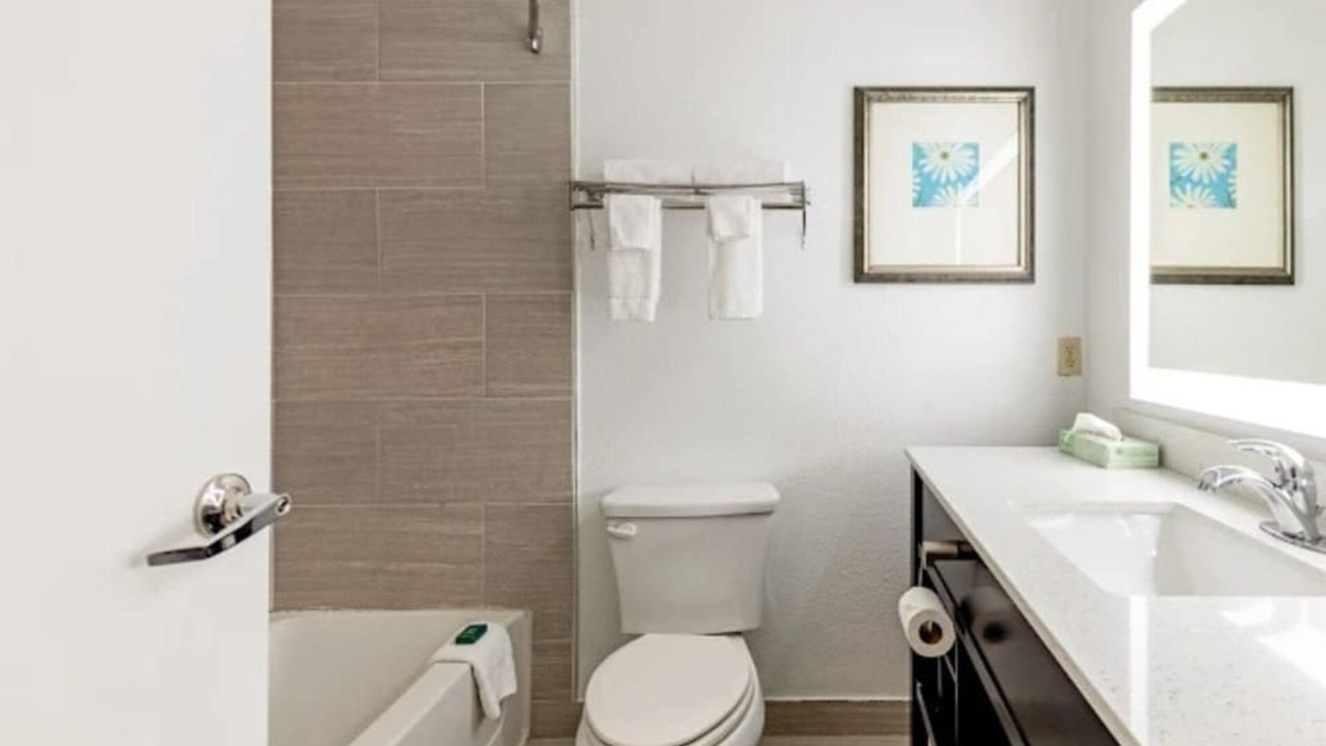 Guest bathroom with bathtub and shower, tiled wall, toilet, towels, vanity, and illuminated mirror at SureStay by Best Western Lewisville Dallas.
