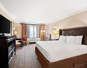 King guest room with white bedding, dark wood furnishings, television, desk, and seating area at Best Western Ontario Mills Mall.