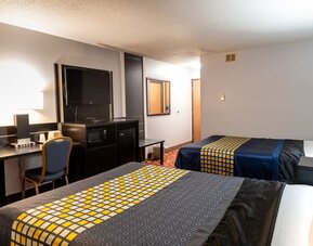 Guest room with two beds, patterned bedding, work desk, television, microwave, and mini refrigerator at Coratel Inn & Suites By Jasper Hastings.
