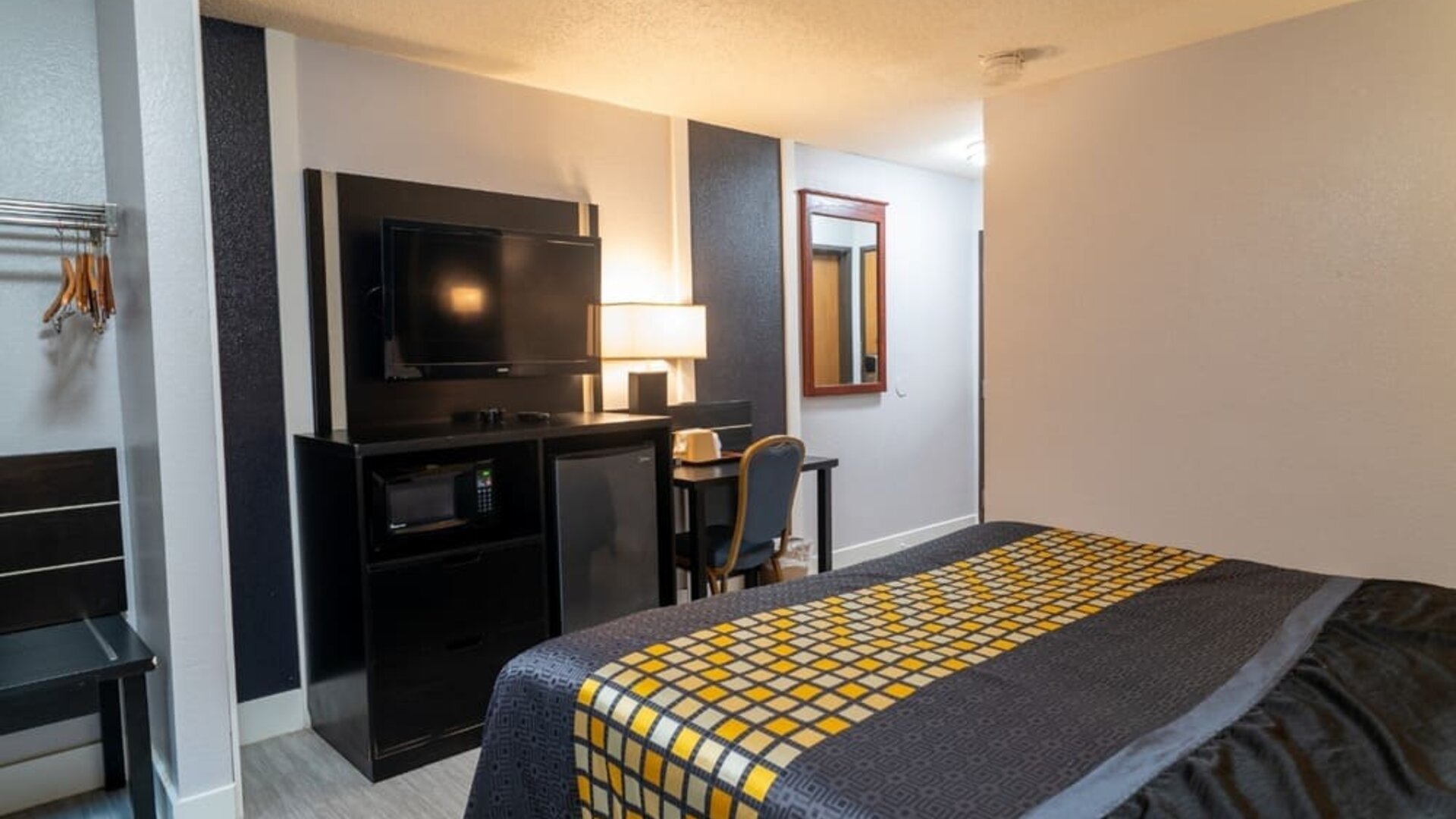 Guest room with bed, television, microwave, mini refrigerator, work desk, and open hanging space at Coratel Inn & Suites By Jasper Hastings.