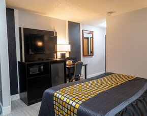 Guest room with bed, television, microwave, mini refrigerator, work desk, and open hanging space at Coratel Inn & Suites By Jasper Hastings.
