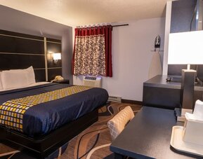 King guest room with patterned bedding, work desk, window, and in-room ironing facilities at Coratel Inn & Suites By Jasper Hastings.