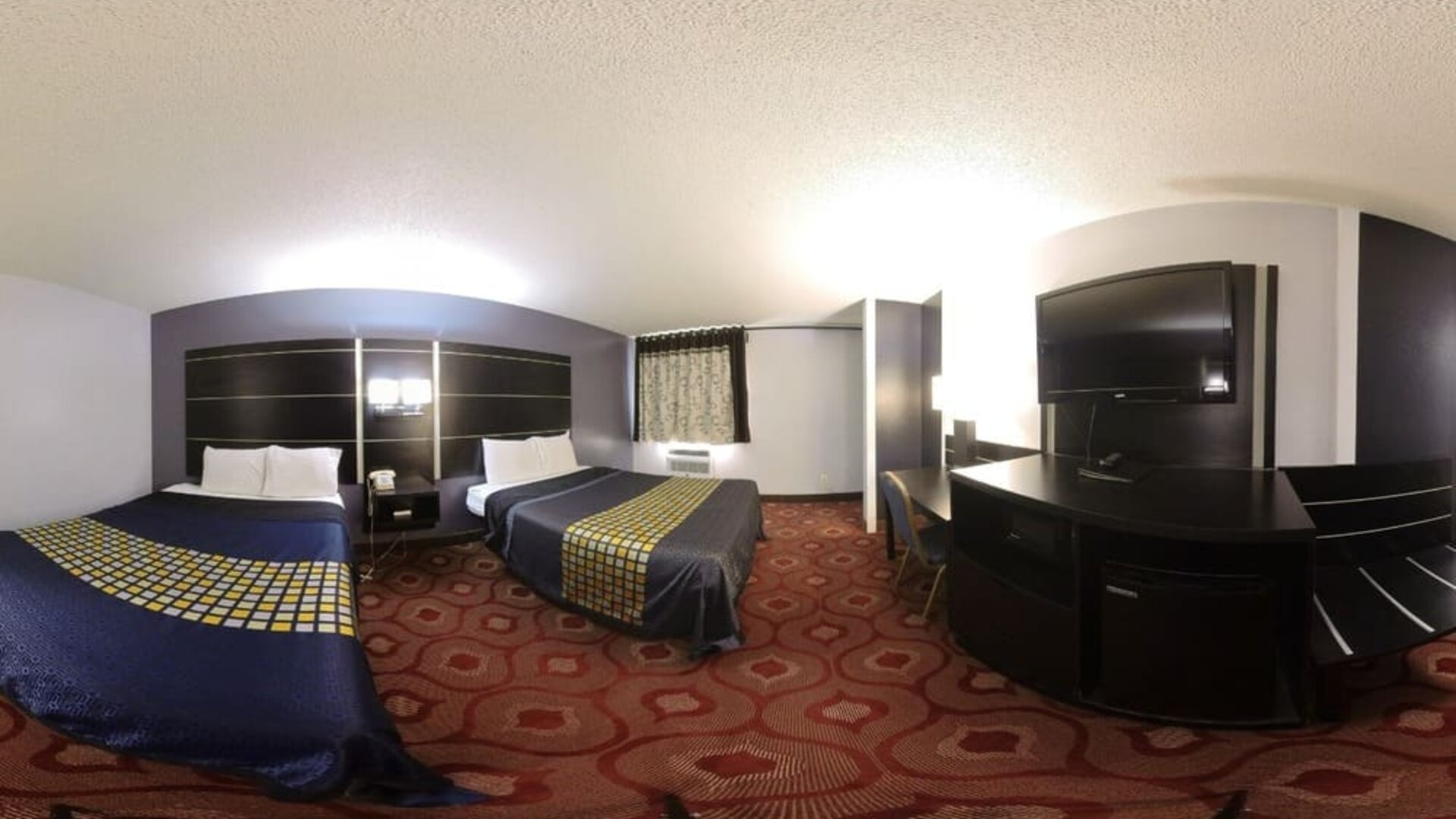 Spacious guest room with two beds, television, work desk, microwave, mini refrigerator, and patterned carpeting at Coratel Inn & Suites By Jasper Hastings.