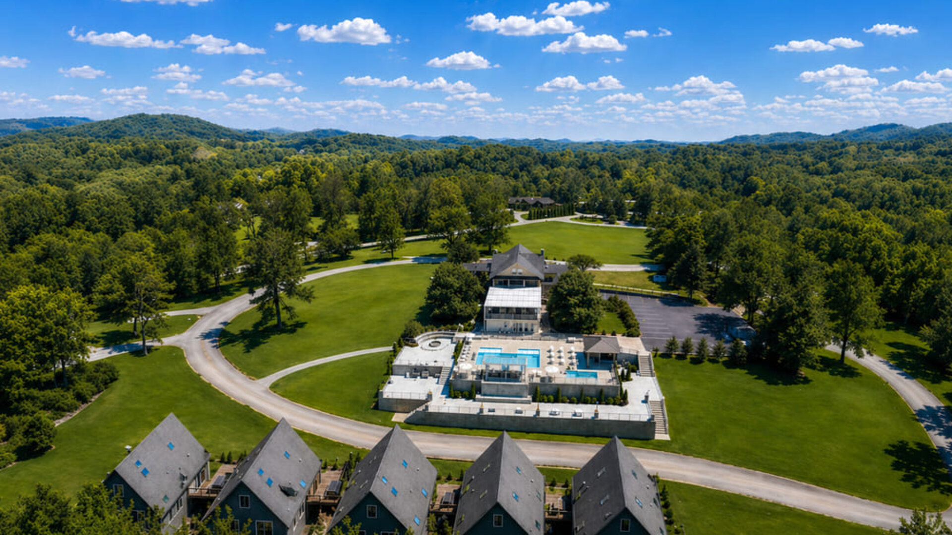 Aerial view of SKYLARANNA Resort & Spa featuring guest buildings, expansive green grounds, swimming pools, and surrounding woodland.