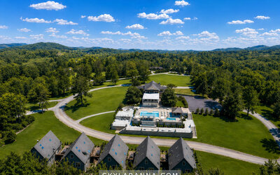 Aerial view of SKYLARANNA Resort & Spa featuring guest buildings, expansive green grounds, swimming pools, and surrounding woodland.