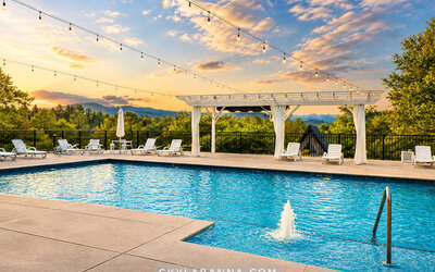 Outdoor swimming pool at sunset with sun loungers, a white pergola, string lights, and scenic mountain views at SKYLARANNA Resort & Spa.