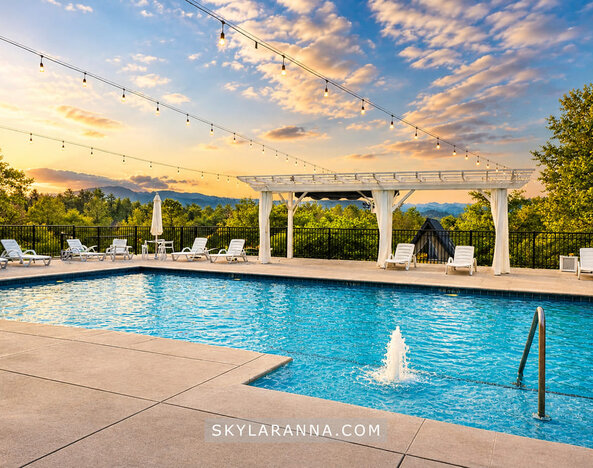 Outdoor swimming pool at sunset with sun loungers, a white pergola, string lights, and scenic mountain views at SKYLARANNA Resort & Spa.