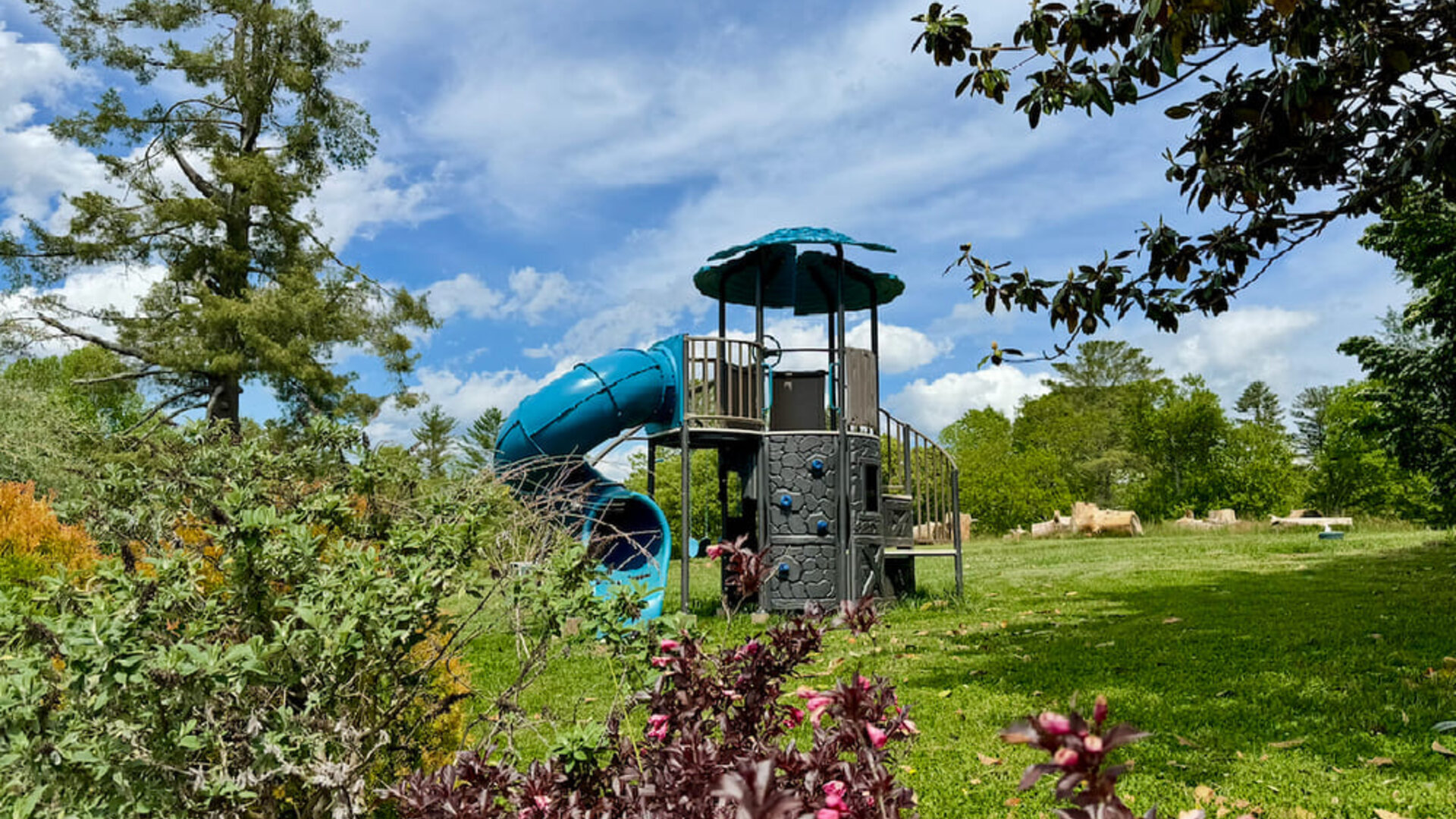 Resort grounds featuring a children's playground with a tube slide surrounded by lawn, trees, and landscaped gardens at SKYLARANNA Resort & Spa.