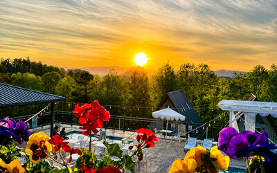Scenic sunset view over the pool area and surrounding mountains, framed by colourful flowers at SKYLARANNA Resort & Spa.