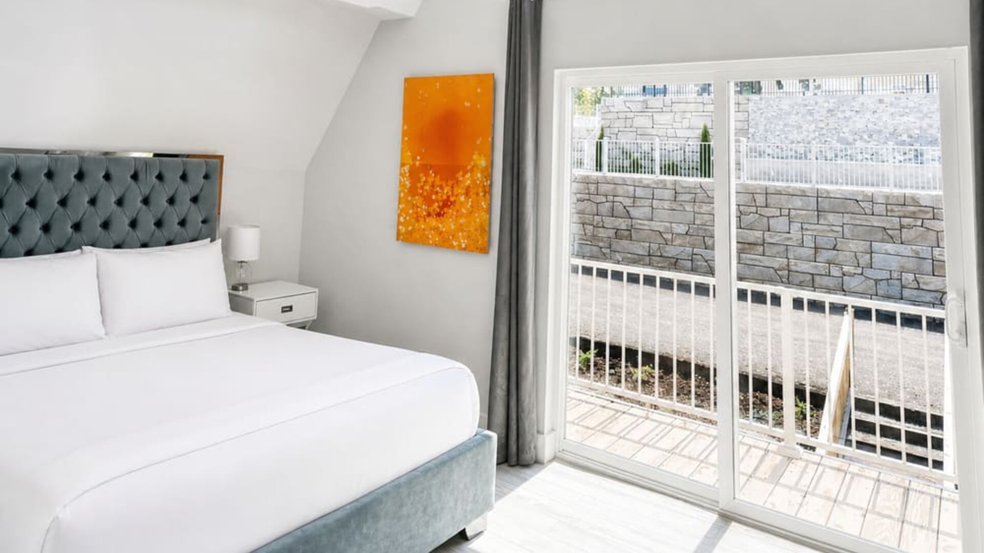 Bright cabin bedroom at SKYLARANNA Resort & Spa, featuring a queen bed, tufted headboard, colourful artwork, vaulted ceiling, and sliding glass doors.