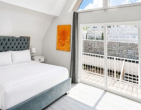 Bright cabin bedroom at SKYLARANNA Resort & Spa, featuring a queen bed, tufted headboard, colourful artwork, vaulted ceiling, and sliding glass doors.