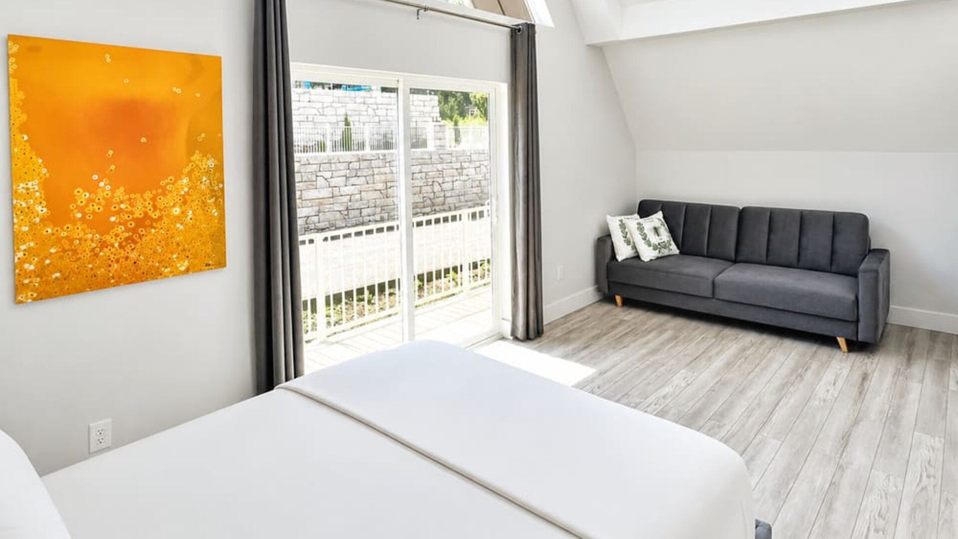 Cabin bedroom and sitting area at SKYLARANNA Resort & Spa, featuring a queen bed, sofa, vaulted ceiling, colourful artwork, and sliding doors providing natural light.