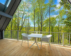 Private wooden balcony at SKYLARANNA Resort & Spa, furnished with a table and chairs and overlooking the surrounding woodland.