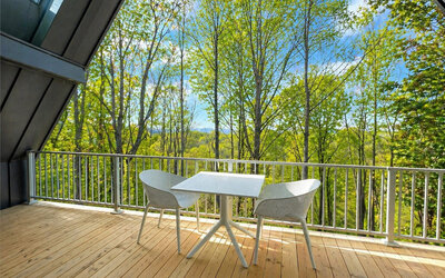 Private wooden balcony at SKYLARANNA Resort & Spa, furnished with a table and chairs and overlooking the surrounding woodland.