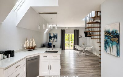 Modern cabin kitchen and open-plan interior at SKYLARANNA Resort & Spa, featuring white cabinetry, an island with sink, dining area, spiral staircase, and contemporary décor.