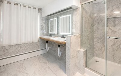 Spacious cabin bathroom at SKYLARANNA Resort & Spa, featuring double sinks, illuminated mirrors, marble-style finishes, and a glass-enclosed shower.