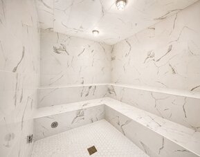 Steam room featuring marble-effect walls, built-in bench seating, and a bright contemporary interior at SKYLARANNA Resort & Spa.