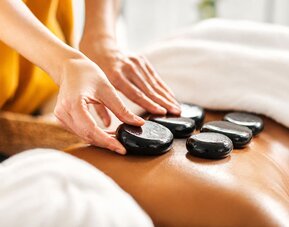 Hot stone massage treatment featuring heated stones placed along a guest's back at SKYLARANNA Resort & Spa.