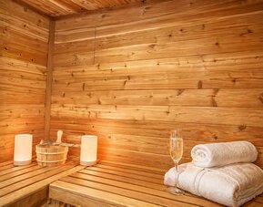 Wood-panelled sauna featuring bench seating, fresh towels, sauna accessories, and ambient lighting at SKYLARANNA Resort & Spa.