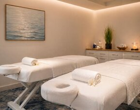 Spa treatment room featuring two massage tables, fresh towels, soft lighting, and contemporary décor at SKYLARANNA Resort & Spa.