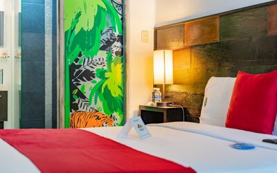 Bright guest room featuring a large bed, exposed brick accent wall, colourful cushions, television, and abundant natural light at Casa Anzures Suites.