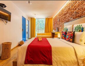 Guest room featuring a comfortable bed, colourful wood-panelled headboard, vibrant tropical artwork, and warm bedside lighting at Casa Anzures Suites.