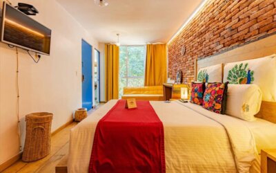Guest room featuring a comfortable bed, colourful wood-panelled headboard, vibrant tropical artwork, and warm bedside lighting at Casa Anzures Suites.