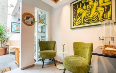 Welcoming common area featuring green lounge chairs, colourful artwork, and a guest refreshment station at Casa Anzures Suites.