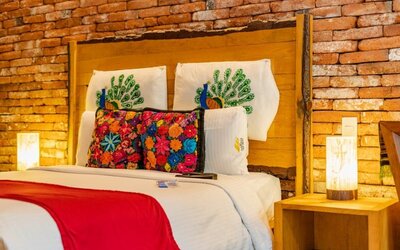 Guest room featuring a large bed, exposed brick accent wall, colourful decorative cushions, and warm bedside lighting at Casa Anzures Suites.