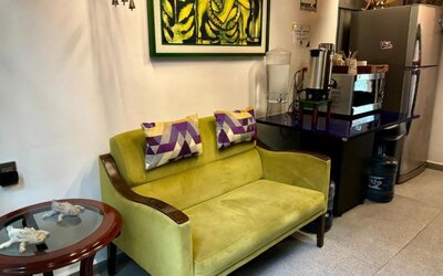 Cosy lounge area featuring a green sofa, decorative cushions, refreshment facilities, and colourful artwork at Casa Anzures Suites.