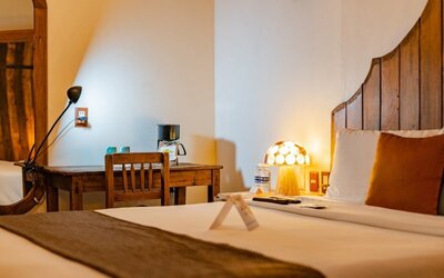 Guest room featuring a comfortable bed, rustic wooden furnishings, bedside lighting, and a dedicated workspace at Casa Anzures Suites.