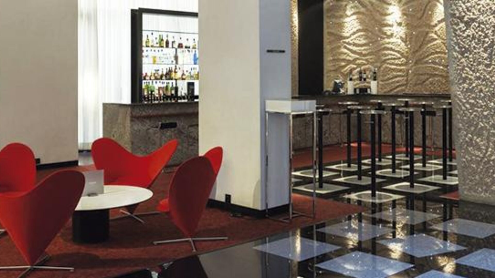 Contemporary bar and lounge featuring vibrant red seating, high-top bar stools, and a well-stocked bar at Hilton Madrid Aeropuerto.