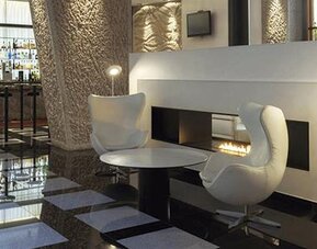 Stylish lounge area featuring contemporary white seating, a modern fireplace, and easy access to the hotel bar at Hilton Madrid Aeropuerto.