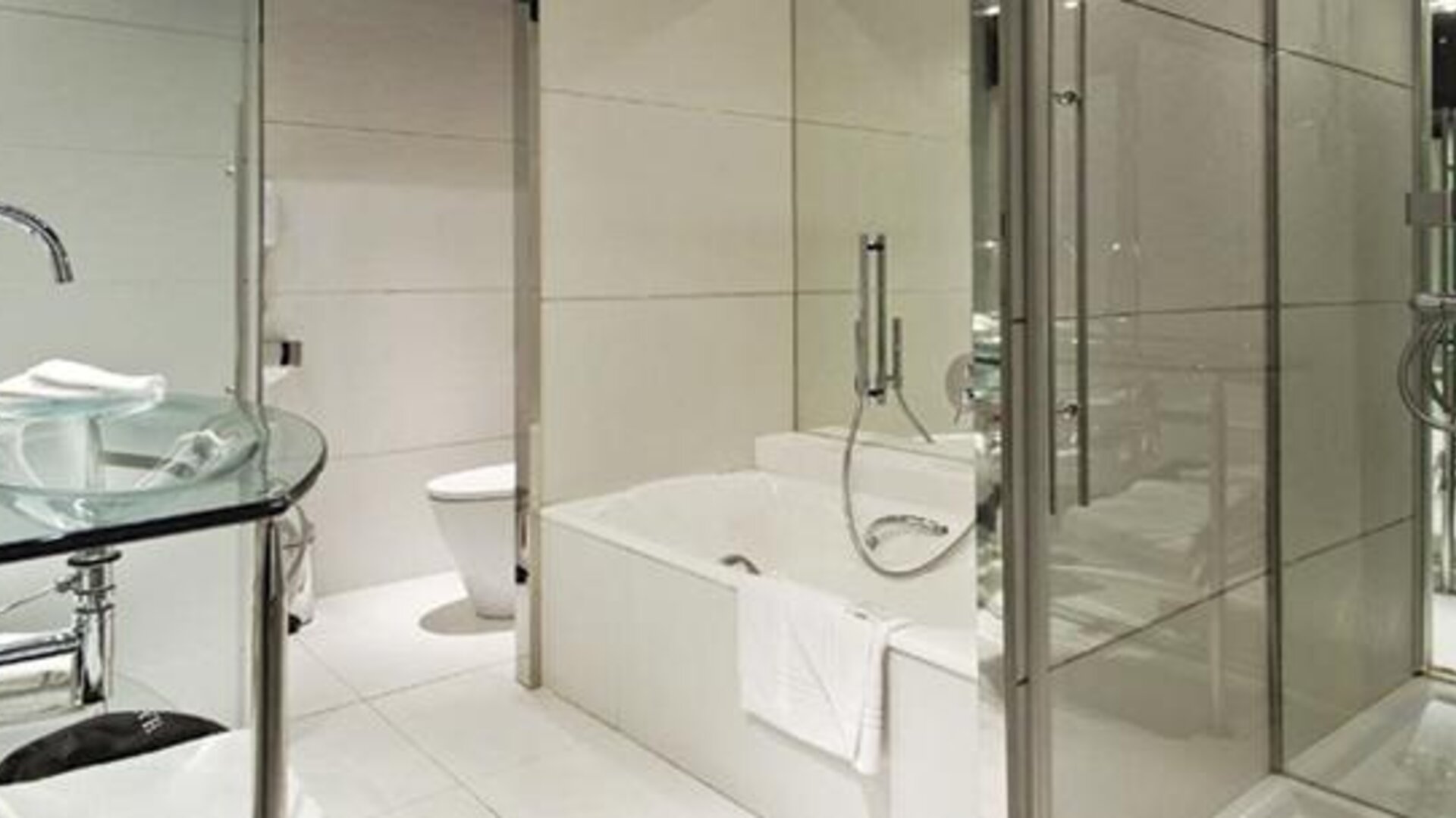 Modern guest bathroom featuring a glass vanity, bathtub, separate glass-enclosed shower, and sleek chrome fixtures at Hilton Madrid Aeropuerto.