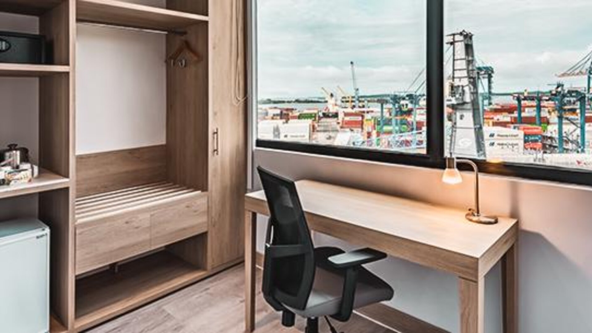 In-room workspace featuring a desk, ergonomic chair, coffee station, mini-fridge, and large window overlooking the port at Holiday Inn Express Cartagena Manga.